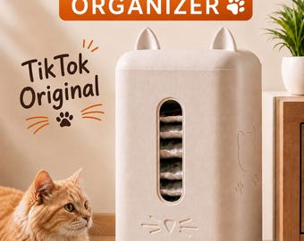 Peut inclure: Un distributeur de nourriture pour animaux beige de forme rectangulaire avec des oreilles de chat sur le dessus, une fenêtre verticale et une fente de distribution. Il porte les inscriptions PET FOOD ORGANIZER et TikTok Original.