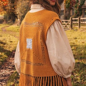 Könnte beinhalten: Eine senfgelbe Häkelweste mit quadratischem Muster und weißer Mitte, ärmellosem Design und langen Fransen am Saum. Die Weste wird über einem cremefarbenen Langarmhemd getragen und mit einem rostfarbenen Hut mit breiter Krempe kombiniert.