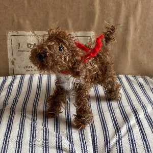 May include: A brown and white plush toy dog wearing a red scarf. The dog is standing on a white and blue striped fabric.
