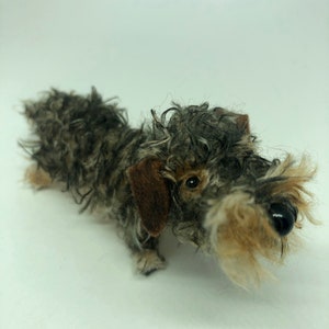 May include: A small, grey and brown wirehaired dachshund soft toy with black button eyes.