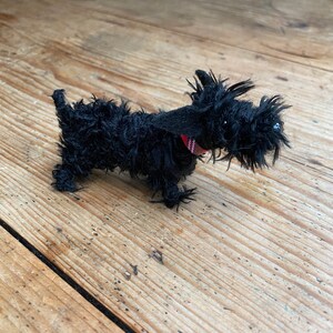 May include: A black plush toy dog with a red and black plaid collar. The dog is standing on a wooden surface.