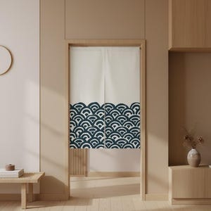 Op de afbeelding: Een crèmekleurig Japans noren-gordijn met een donkerblauw golfpatroon aan de onderkant. Het gordijn hangt in een houten deuropening en voegt een vleugje minimalistische decoratie toe aan de kamer. Het ontwerp is een klassiek Japans motief.