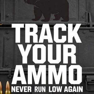 May include: A black graphic print featuring a silhouette of a bear above the white text TRACK YOUR AMMO and NEVER RUN LOW AGAIN. Several brass-coloured metallic cartridges are arranged at the bottom against a dark, textured background.