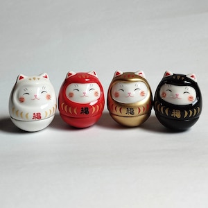 以下が含まれることがあります： 白、赤、金、黒の4体の日本の招き猫の置物。各猫は笑顔で、赤または金の首輪をしており、お腹には「幸運」の漢字が書かれています。置物は楕円形で、光沢のある仕上がりです。