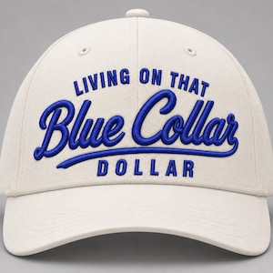 Puede incluir: Una gorra de béisbol de color crema con el texto azul bordado "LIVING ON THAT Blue Collar DOLLAR" en la parte delantera. La gorra tiene una corona estructurada, una visera curva y ojales cosidos en los paneles superiores para ventilación.