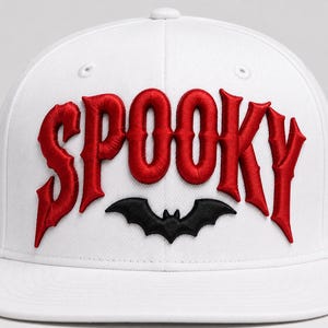 Op de afbeelding: Een witte baseballpet met het woord SPOOKY geborduurd in dikke, rode letters in gotische stijl op de voorpanelen. Onder de tekst is een kleine zwarte vleermuis-silhouet in het midden geborduurd, wat een opvallend grafisch detail toevoegt.
