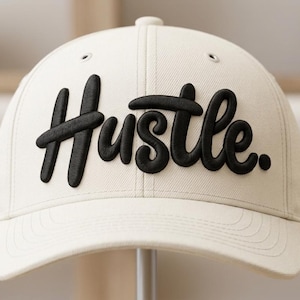 Może przedstawiać: Kremowa czapka bejsbolowa z napisem "Hustle" wyhaftowanym pogrubioną, czarną czcionką z przodu. Czapka ma zakrzywiony daszek i guzik na górze.