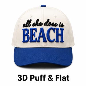 Puede incluir: Gorra de béisbol con corona color crema y visera azul. La gorra presenta la frase bordada "all she does is BEACH" en negro y azul. El texto "3D Puff & Flat" está debajo.