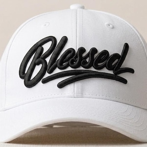 May include: A white baseball cap featuring the word "Blessed" in black, cursive lettering. The cap has a curved peak and a button on the crown. A simple, stylish accessory.