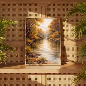 May include: A framed landscape painting depicting a serene river scene. The artwork features a river flowing through a forest with trees in autumn colors. The painting is displayed on a wooden shelf against a woven background.