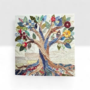 May include: A textile artwork depicting a tree. The trunk is brown and blue, with colourful fabric leaves and flowers. Decorative buttons are used throughout the design. The background is a patchwork of neutral-toned fabrics.