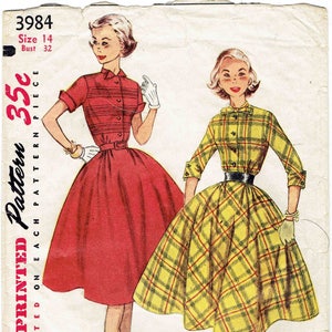 Può includere: Modello di cucito vintage Simplicity per un abito, con due modelle che indossano diverse versioni dell'abito. L'abito a sinistra è rosso con un colletto bianco e maniche corte. L'abito a destra è giallo e a quadri con una cintura nera e maniche corte. Il numero del modello è 3984, taglia 14, seno 81 cm. Il modello costa 35 centesimi.