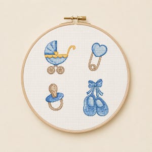 Può includere: Un telaio da ricamo a punto croce con disegni a tema baby. I disegni includono un passeggino blu, una spilla da balia a forma di cuore, un ciuccio e scarpine da neonato. Il ricamo è realizzato in tonalità blu e oro su sfondo bianco.