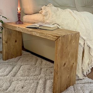 May include: A rustic wooden bench with a natural finish. A book and glasses rest on the bench's surface, alongside a lit candle in a decorative holder. The bench is approximately 100 cm long.