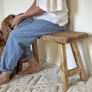 May include: A rustic wooden bench with a natural finish. The bench has a rectangular seat and four sturdy legs. The wood grain is visible, giving it a warm, inviting look. The bench is approximately 36 inches long.