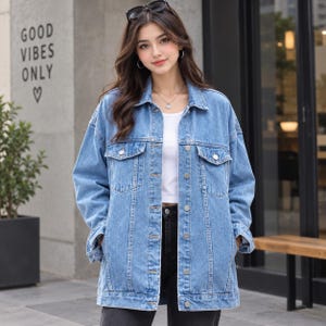 Op de afbeelding: Een medium-wash blauw spijkerjack met een klassieke kraag, lange mouwen, twee borstzakken met knoopsluiting en een knoopsluiting aan de voorzijde. Het jack wordt gedragen over een effen wit shirt en een donkere broek, met een relaxte pasvorm.