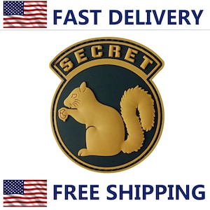 May include: A round emblem with a gold squirrel silhouette on a dark teal background, framed by a gold border and the word "SECRET". The image includes the text "FAST DELIVERY" and "FREE SHIPPING" with American flags.