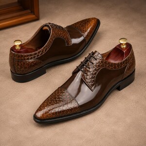May include: A pair of brown leather dress shoes with a glossy finish. The shoes feature a textured, reptile-like pattern on the toe and heel, with a smooth, polished leather upper. The shoes have laces and are displayed with wooden shoe trees.