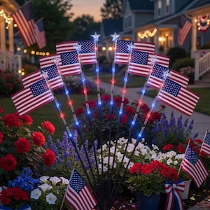 May include: A nighttime scene of a suburban yard decorated for a patriotic holiday. American flags are displayed in flower beds and along the walkway. Some flags have red, white, and blue lights. Red, white, and blue flowers and decorations are also present.