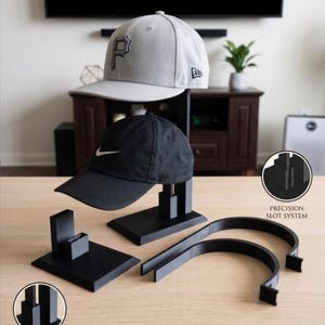 Könnte beinhalten: Ein Dual-Tier-Hut-Schreibtisch-Dock mit Komponenten. Das Bild zeigt eine graue Baseballkappe mit einem schwarzen "P"-Logo und eine schwarze Nike-Kappe. Das Dock ist schwarz und enthält ein Präzisionsschlitzsystem.