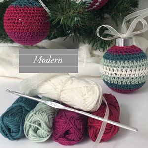 May include: Handmade crocheted Christmas baubles in teal, burgundy, and cream hang from a Christmas tree. The word "Modern" is displayed in a white box. Yarn and a 3.50mm crochet hook are in the foreground, suggesting a craft project.