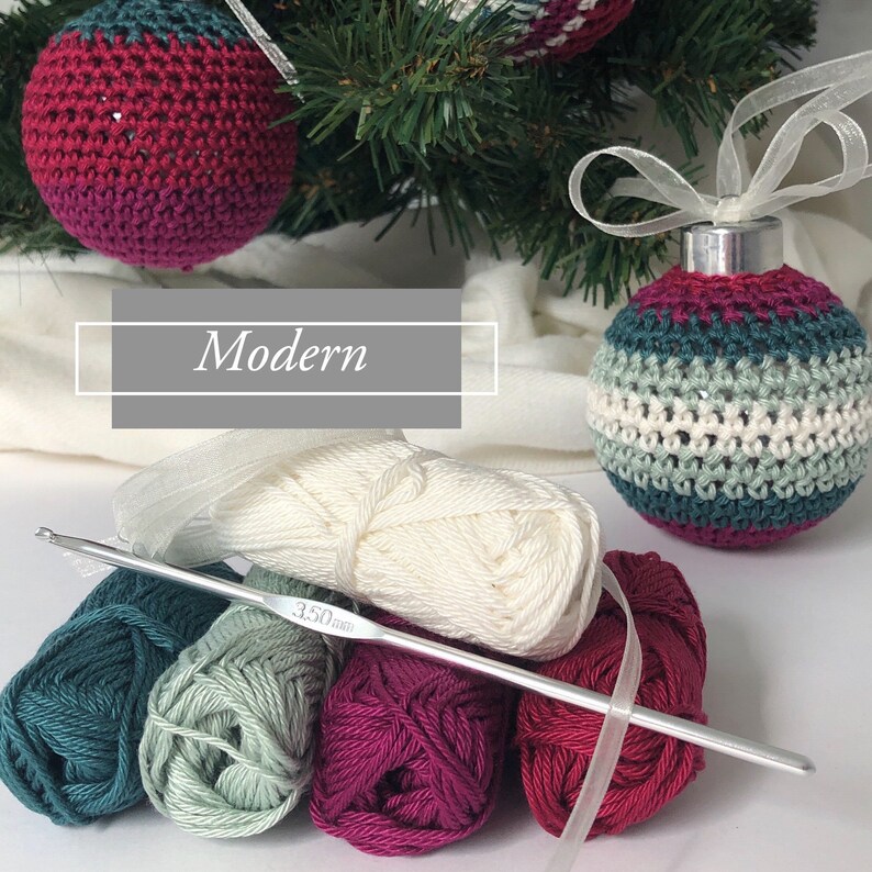 May include: Handmade crocheted Christmas baubles in teal, burgundy, and cream hang from a Christmas tree. The word "Modern" is displayed in a white box. Yarn and a 3.50mm crochet hook are in the foreground, suggesting a craft project.