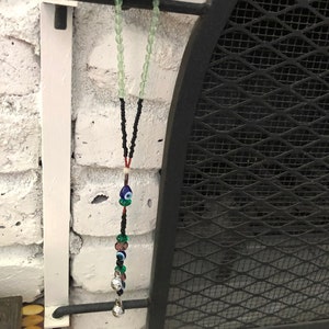 May include: A beaded necklace with a green and black string, and a charm with blue and green evil eyes and silver bells.