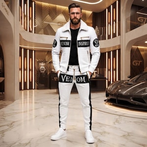 May include: A white jacket with a faux fur collar, black accents, and the text "VENOM INSPIRED" on the chest, paired with matching white trousers featuring a black side stripe and the word "VENOM" printed across the upper thigh area.
