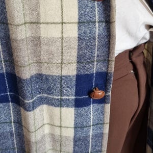 以下が含まれることがあります： 青、ベージュ、白のチェック柄ブレザー。茶色の革ボタンが3つ付いています。白いシャツと茶色のズボンを着用。チェック柄はクラシックなデザインです。