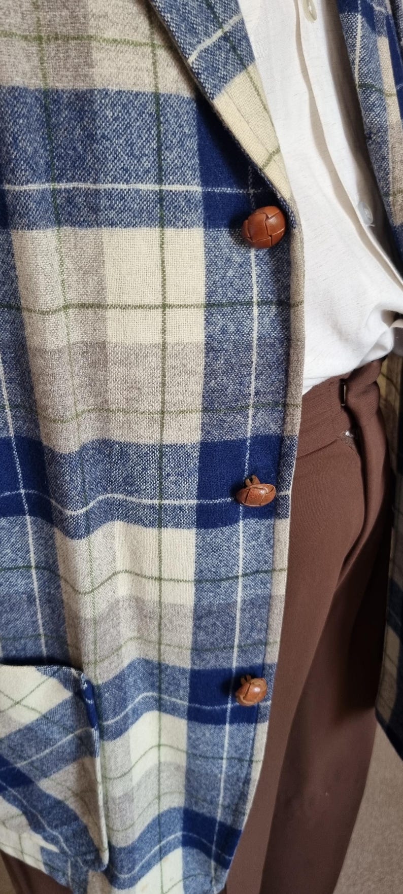 以下が含まれることがあります： 青、ベージュ、白のチェック柄ブレザー。茶色の革ボタンが3つ付いています。白いシャツと茶色のズボンを着用。チェック柄はクラシックなデザインです。