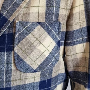 以下が含まれることがあります： 胸ポケット付きの青、白、ベージュのチェック柄ブレザー。 ジャケットは織物でできており、クラシックなデザインです。 ブレザーは白いシャツの上に着用されています。