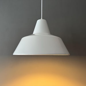 Könnte beinhalten: Eine weiße Pendelleuchte mit konischem Oberteil und ausgestelltem Schirm. Die Leuchte hängt an einem weißen Kabel. Der Hintergrund ist ein Grau-Gelb-Verlauf. Die Leuchte ist für die Deckenaufhängung konzipiert und sorgt für eine Abwärtsbeleuchtung.