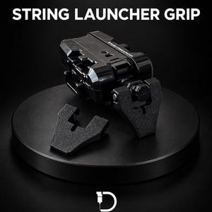 Può includere: Un'impugnatura per lanciatore a corda della serie nera con corpo in plastica nera e attacco per impugnatura testurizzato. Il testo recita BLACK SERIES STRING LAUNCHER GRIP e D.LAB STUDIO 3D PRINTING & CAD DESIGN. Include un pezzo separato.
