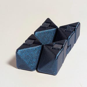 May include: A geometric puzzle toy in shades of dark blue. The puzzle is composed of several interlocking triangular pieces, each with a textured surface and small square details. The toy is designed to be manipulated and reconfigured.