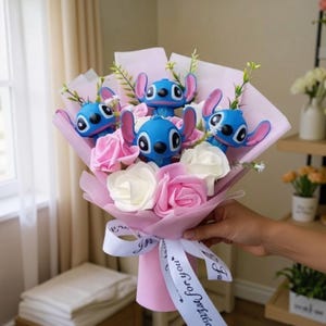 May include: A bouquet featuring blue character figurines with pink ears, interspersed with pink and white artificial roses. The bouquet is wrapped in pink paper and tied with a white ribbon that says "wish for you".