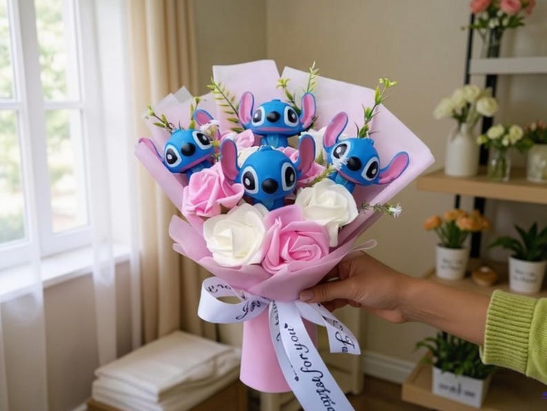May include: A bouquet featuring blue character figurines with pink ears, interspersed with pink and white artificial roses. The bouquet is wrapped in pink paper and tied with a white ribbon that says "wish for you".