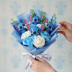 Pu&ograve; includere: Un bouquet con statuette blu di Stitch, rose di stoffa bianche e blu e verde, avvolto in carta blu. Un nastro bianco con la scritta "Just for you" &egrave; legato intorno alla base.