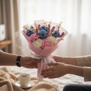 May include: A bouquet featuring blue Stitch plush toys, pink and white roses, and greenery, wrapped in pink paper and tied with a ribbon that says "I love you".