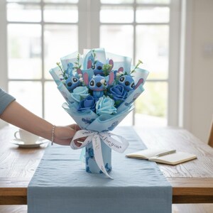 May include: A bouquet featuring blue roses and Stitch character figures, wrapped in blue paper and tied with a ribbon that says "for you". The bouquet is on a wooden table with a blue runner.