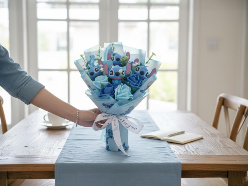 May include: A bouquet featuring blue roses and Stitch character figures, wrapped in blue paper and tied with a ribbon that says "for you". The bouquet is on a wooden table with a blue runner.
