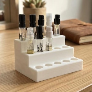 Peut inclure: Un présentoir blanc à gradins doté de plusieurs découpes circulaires conçues pour contenir de petits flacons cylindriques. Le support comporte trois niveaux, avec plusieurs fioles en verre transparent contenant du liquide et des bouchons noirs ou blancs.