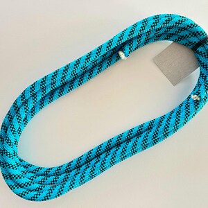Könnte beinhalten: Ein gewickeltes Kletterseil in Türkis- und Schwarztönen mit einem sich wiederholenden diagonalen Muster. Das Seil ist geschlungen und ein kleines Etikett ist angebracht. Das Seil ist für Kletter- und Outdoor-Aktivitäten konzipiert.