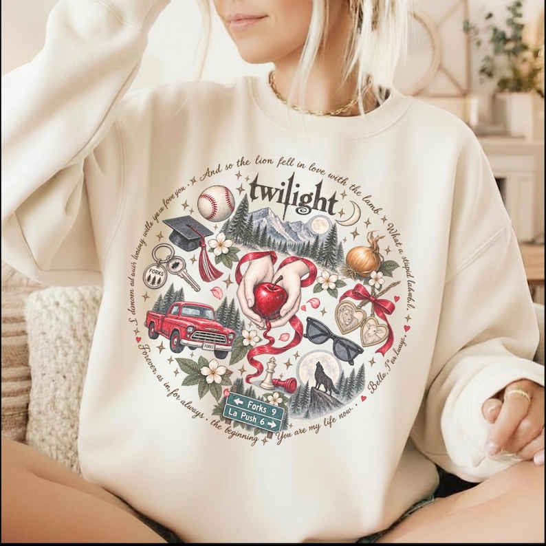 May include: A cream-colored crewneck sweatshirt featuring a circular graphic print. The design includes a red truck, a baseball, a graduation cap, a red apple held by hands, sunglasses, a wolf silhouette, and text reading Twilight and Forks.