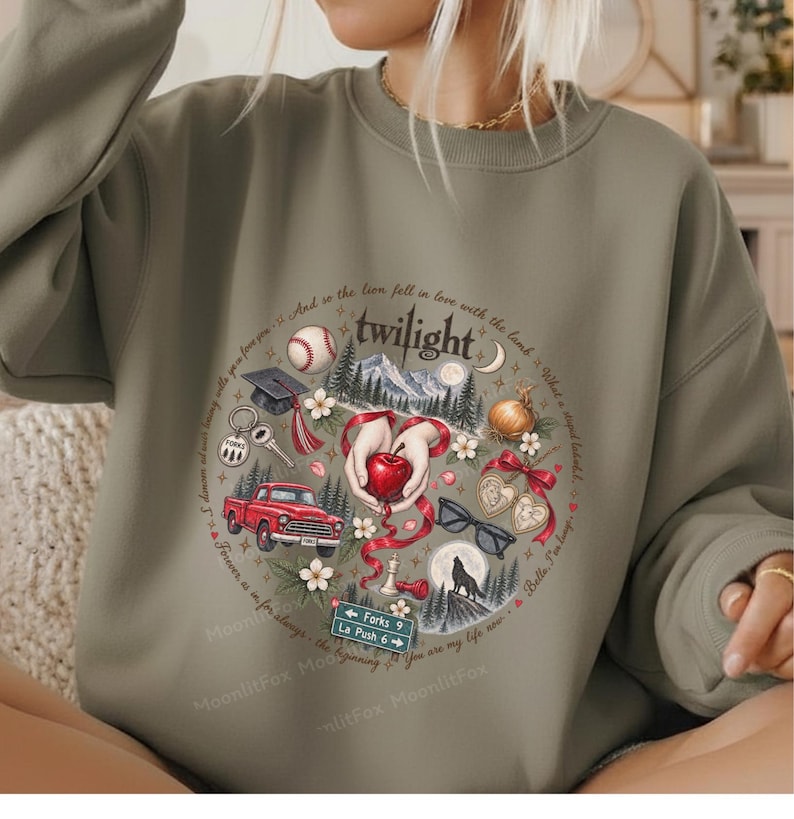 May include: An olive green crewneck sweatshirt featuring a circular graphic print. The design includes a red apple, a red truck, a baseball, a graduation cap, a wolf silhouette, sunglasses, and a sign reading Forks 9 La Push 6.