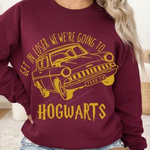 May include: A maroon long-sleeve sweatshirt featuring a yellow graphic of a vintage car. The text reads GET IN LOSER WE'RE GOING TO HOGWARTS, with the license plate 7990 TD visible on the front bumper of the illustrated vehicle.