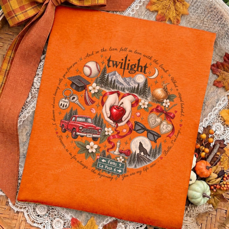 May include: An orange fabric item featuring a circular graphic with the text Twilight. The design includes a baseball, graduation cap, red truck, hands holding an apple, sunglasses, a wolf silhouette, and a road sign reading Forks 9 La Push 6.