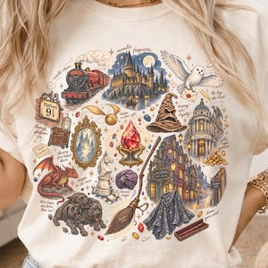 Może przedstawiać: Kremowy t-shirt z nadrukiem przedstawiającym magiczne elementy, w tym czerwony pociąg parowy, zamek, białą sowę, tiarę przydziału, smoka, trzygłowego psa, miotłę, lustro oraz różne napisy w języku angielskim rozmieszczone wokół grafiki.