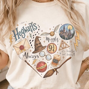 May include: A cream-colored t-shirt featuring a heart-shaped graphic collage of wizarding world icons, including a sorting hat, a castle, a broomstick, a golden snitch, a letter, glasses, a mug of butterbeer, and text reading Hogwarts, Always, Muggles, 9 3/4, and it's levioSa, not leviosA.