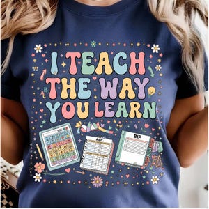 May include: A navy blue t-shirt featuring the text I TEACH THE WAY YOU LEARN in colorful, retro-style bubble letters. The design includes illustrations of a tablet with icons, a spiral-bound notebook labeled ABC, and a document labeled BIP.