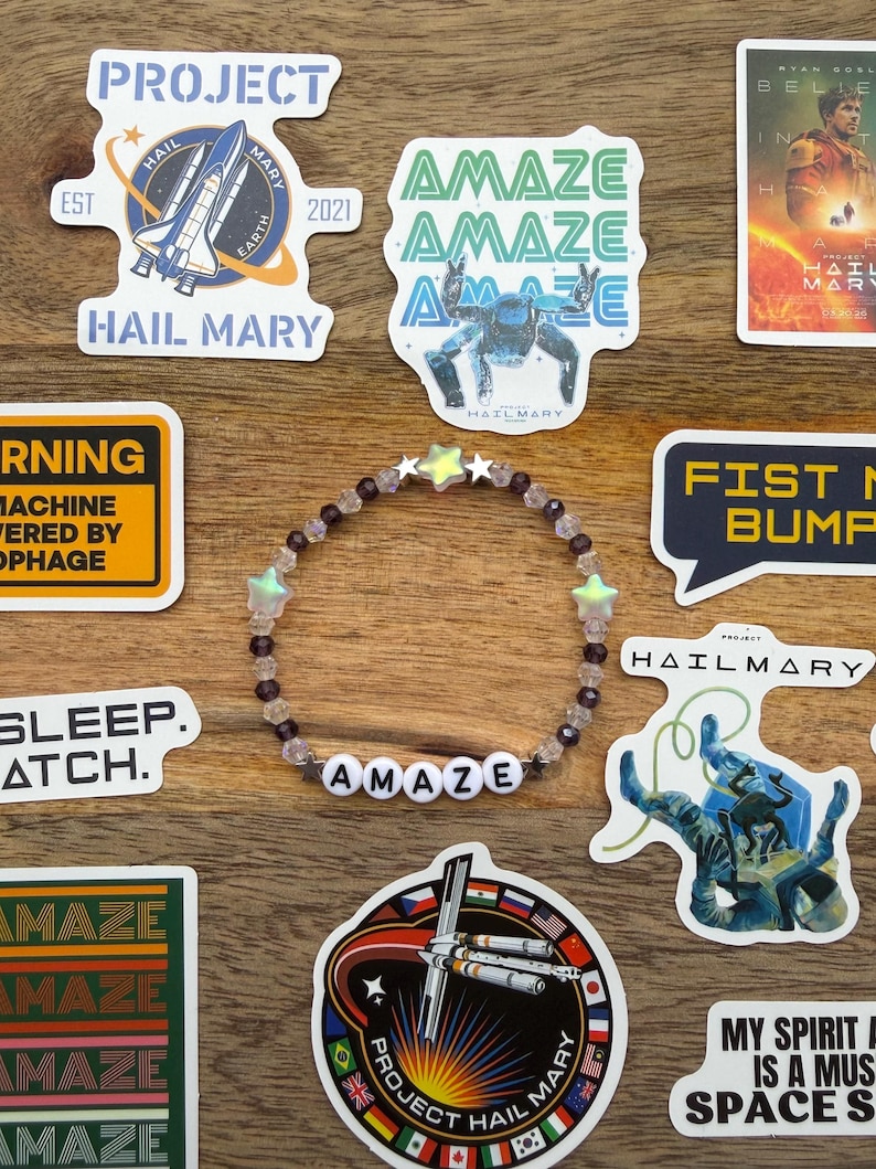 May include: A collection of stickers and a beaded bracelet with the word "AMAZE". The stickers feature space-themed designs, including a spaceship, a robot, and text that reads "Project Hail Mary". The bracelet has star-shaped beads.